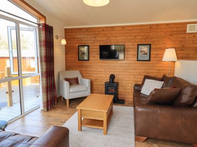 A living room with a brown leather sofa a grey armchair a wooden coffee table and a wall-mounted TV at Ramblers Rest Lodge Pinewood 22 Limefitt Park near Windermere