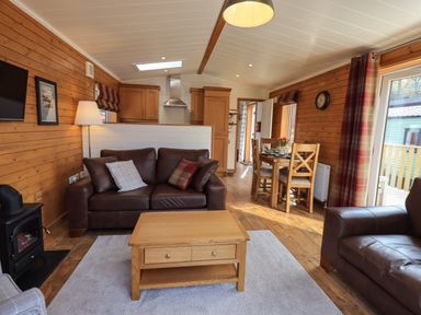 A living room with leather sofas a wooden coffee table and a dining table at Ramblers Rest Lodge Pinewood 22 Limefitt Park near Windermere