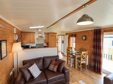 A living room and kitchen with brown leather sofa and wooden dining table at Ramblers' Rest Lodge Pinewood 22 Limefitt Park near Windermere