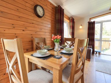 A dining area with a wooden table set for four with bowls glasses and a vase of flowers at Ramblers Rest Lodge Pinewood 22 Limefitt Park near Windermere