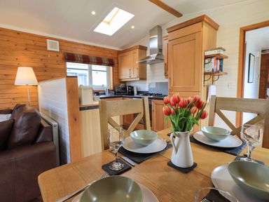 A kitchen and dining area with wooden furniture and red flowers on the table at Ramblers Rest Lodge Pinewood 22 Limefitt Park near Windermere