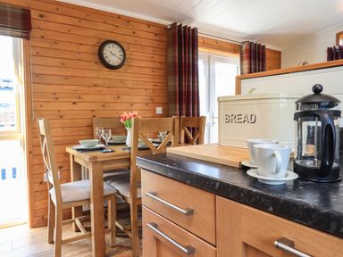 A dining area with a wooden table set for four and kitchen counter with a bread bin and coffee maker at Ramblers Rest Lodge Pinewood 22 Limefitt Park near Windermere