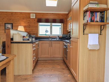 A kitchen with wooden cabinets a countertop with a bread container and coffee maker and a window above the sink at Ramblers Rest Lodge Pinewood 22 Limefitt Park near Windermere