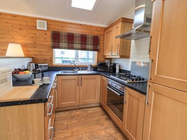 A kitchen with wooden cabinets a gas stove and a window with a plaid blind at Ramblers Rest Lodge Pinewood 22 Limefitt Park near Windermere