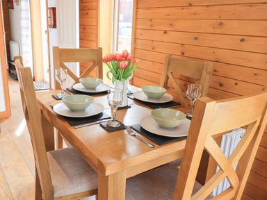 A wooden dining table set for four with plates bowls glasses and a vase of flowers at Ramblers' Rest Lodge Pinewood 22 Limefitt Park near Windermere