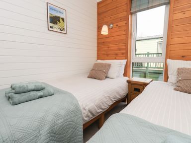 A bedroom with two single beds a nightstand window and folded towels at Ramblers Rest Lodge Pinewood 22 Limefitt Park near Windermere