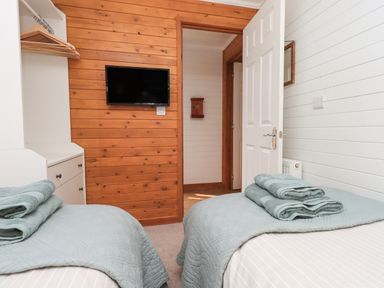 A bedroom with two single beds with green towels on them a TV mounted on a wooden wall and a white closet Ramblers Rest Lodge Pinewood 22 Limefitt Park near Windermere