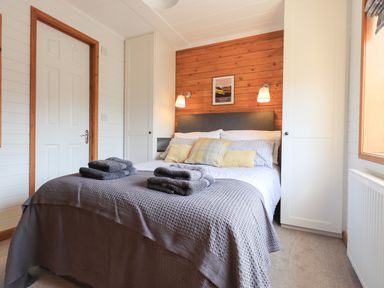 A bedroom with a double bed towels on bed built-in wardrobes and wall lamps at Ramblers Rest Lodge Pinewood 22 Limefitt Park near Windermere