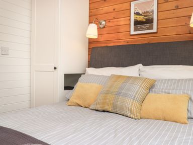 A bedroom with a bed with grey and white linens and yellow cushions and a white wardrobe Ramblers Rest Lodge Pinewood 22 Limefitt Park near Windermere
