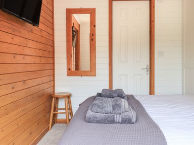 A bedroom with a bed covered in towels a wooden stool a wall mirror and a wall-mounted TV at Ramblers Rest Lodge Pinewood 22 Limefitt Park near Windermere