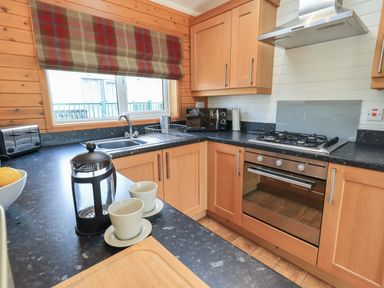 A kitchen with wooden cabinets a gas stove a toaster a microwave a French press and cups at Ramblers Rest Lodge Pinewood 22 Limefitt Park near Windermere