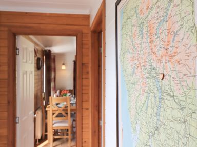 A hallway with a framed map on the wall and a view into a dining area with a table and chairs at Ramblers Rest Lodge in Pinewood 22 Limefitt Park near Windermere