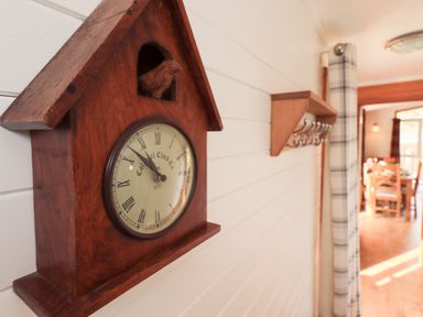 A wooden cuckoo clock mounted on a white paneled wall with a shelf and hooks nearby at Ramblers Rest Lodge Pinewood 22 Limefitt Park near Windermere