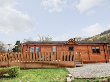 A wooden cabin with a fenced deck and patio umbrella on grass and gravel at Ramblers Rest Lodge Pinewood 22 Limefitt Park near Windermere