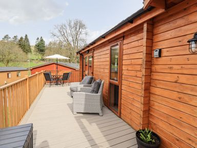 A wooden deck with two cushioned chairs a table with four chairs and an umbrella at Ramblers Rest Lodge Pinewood 22 Limefitt Park near Windermere