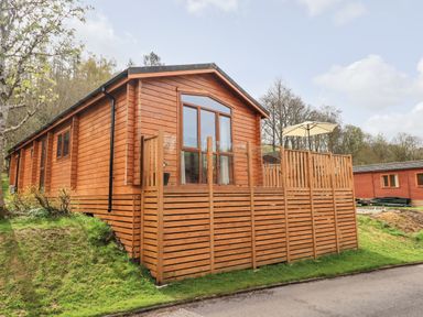 A wooden cabin with a deck and umbrella at Ramblers Rest Lodge in Pinewood 22 Limefitt Park near Windermere