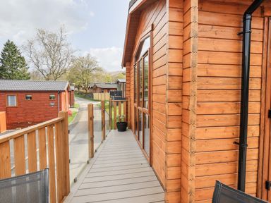 A wooden balcony with glass panels and a potted plant outside a wooden lodge at Ramblers Rest Lodge Pinewood 22 Limefitt Park near Windermere