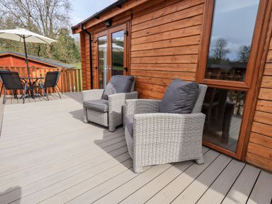 A wooden deck with two wicker armchairs and a table with chairs and umbrella at Ramblers Rest Lodge in Pinewood 22 Limefitt Park near Windermere