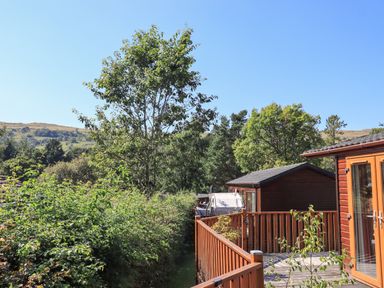 A wooden deck with railings and a small wooden cabin surrounded by trees and hills at Striding Edge Lodge Ullswater 9 Limefitt Park near Windermere