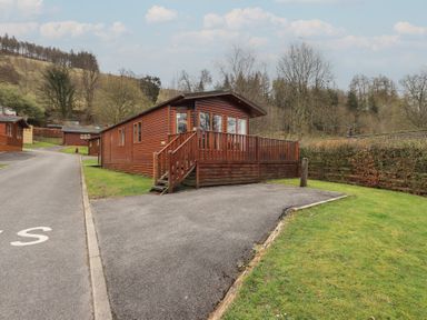 A wooden lodge with a small deck and stairs beside a paved driveway surrounded by grass at Striding Edge Lodge Ullswater 9 Limefitt Park near Windermere