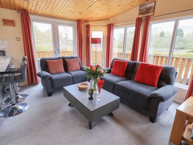 A living room with two grey sofas and a coffee table with flowers at Striding Edge Lodge Ullswater 9 Limefitt Park near Windermere