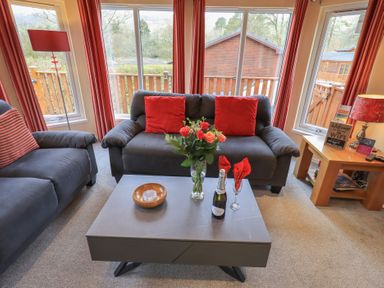 A living room with two gray sofas with red cushions and a gray coffee table with flowers and a bottle at Striding Edge Lodge Ullswater 9 Limefitt Park near Windermere