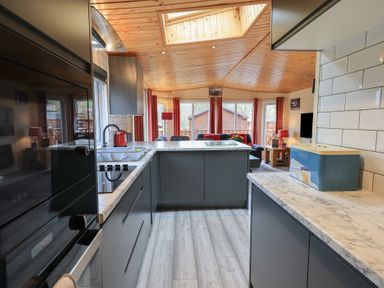 A kitchen with grey cabinets a marble countertop a blue bread box and a view of the living room at Striding Edge Lodge Ullswater 9 Limefitt Park near Windermere