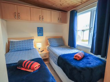 A bedroom with two single beds blue bedding wooden cabinets and a small bedside table at Striding Edge Lodge Ullswater 9 Limefitt Park near Windermere