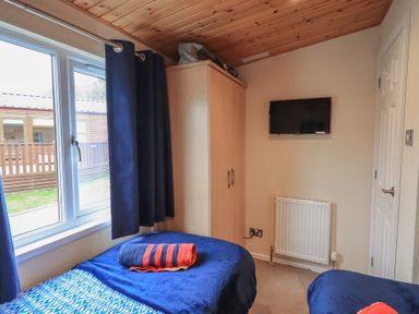 A bedroom with two single beds a wardrobe a wall-mounted television and a window with blue curtains at Striding Edge Lodge Ullswater 9 Limefitt Park near Windermere