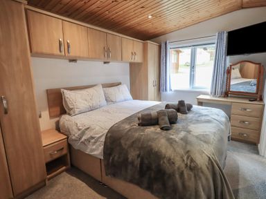 A bedroom with a double bed towels on bed wooden cupboards and a dressing table with a mirror at Striding Edge Lodge Ullswater 9 Limefitt Park near Windermere