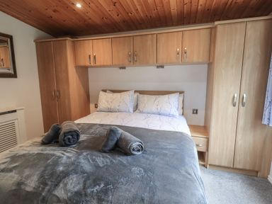 A bedroom with a bed with pillows and rolled towels and wooden wardrobes and overhead cabinets at Striding Edge Lodge Ullswater 9 Limefitt Park near Windermere
