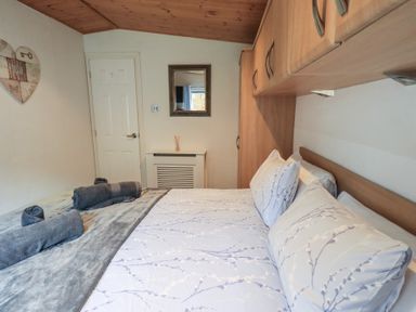 A bedroom with a bed covered in patterned bedding towels on the bed a door a mirror and wooden cabinets on the wall at Striding Edge Lodge Ullswater 9 Limefitt Park near Windermere