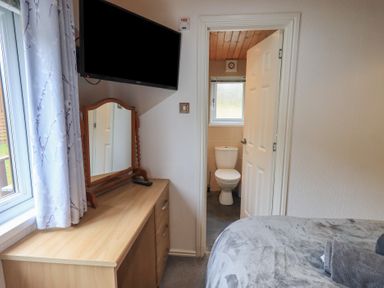 A bedroom with a dresser mirror a wall-mounted TV a bed and a door leading to a bathroom at Striding Edge Lodge Ullswater 9 Limefitt Park near Windermere
