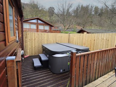 An outdoor hot tub with steps on a wooden deck next to a wooden fence and cabin at Striding Edge Lodge Ullswater 9 Limefitt Park near Windermere