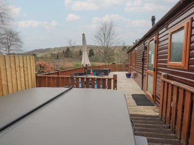 An outdoor deck area with a hot tub seating area with a table and umbrella next to a wooden cabin at Striding Edge Lodge Ullswater 9 Limefitt Park near Windermere