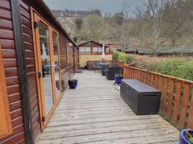 A wooden deck with outdoor furniture and planters outside wooden cabins at Striding Edge Lodge Ullswater 9 Limefitt Park near Windermere
