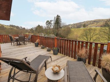 A wooden deck with lounge chairs a table with chairs and potted plants overlooking hills and trees at Horseshoe Lodge Wansfell 5 Limefitt Park near Windermere