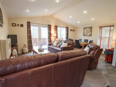 A living room with brown leather sofas a coffee table a dining table with chairs and large windows at Horseshoe Lodge Wansfell 5 Limefitt Park near Windermere