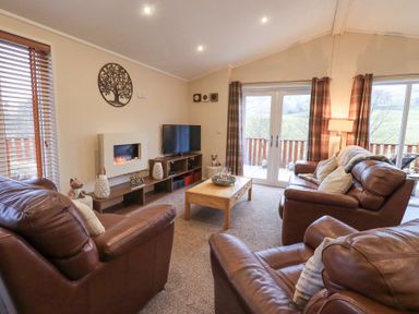 A living room with brown leather sofas a wooden coffee table a wall-mounted fireplace and a television at Horseshoe Lodge Wansfell 5 Limefitt Park near Windermere