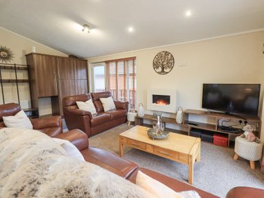A living room with brown leather sofas a wooden coffee table a wall-mounted electric fireplace a flat-screen TV on a wooden stand and decorative wall art at Horseshoe Lodge Wansfell 5 Limefitt Park near Windermere