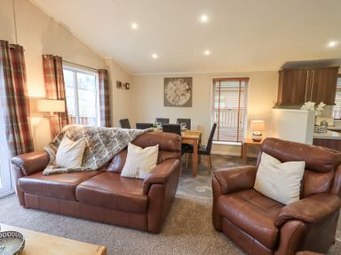 A living room with brown leather sofas a wooden dining table with chairs and a kitchen area at Horseshoe Lodge in Wansfell 5 Limefitt Park near Windermere
