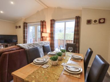 A dining table with plates glasses and plants next to a living area with a sofa and television at Horseshoe Lodge in Wansfell 5 Limefitt Park near Windermere