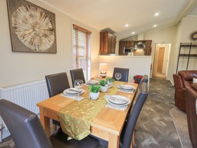 A dining area with a wooden table set with plates and glasses near a kitchen with wooden cabinets at Horseshoe Lodge Wansfell 5 Limefitt Park near Windermere