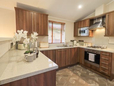 A kitchen with wooden cabinets white countertops a stainless steel oven and microwave and a window with blinds at Horseshoe Lodge Wansfell 5 Limefitt Park near Windermere