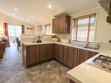 A kitchen with wooden cabinets a sink a gas stove and an open view to a dining area and living room at Horseshoe Lodge Wansfell 5 Limefitt Park near Windermere