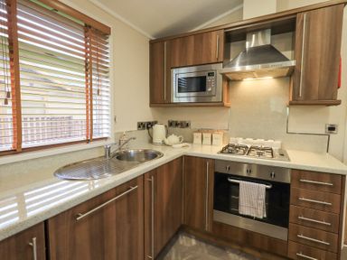 A kitchen with wooden cabinets a microwave stove teapot and kettle at Horseshoe Lodge Wansfell 5 Limefitt Park near Windermere