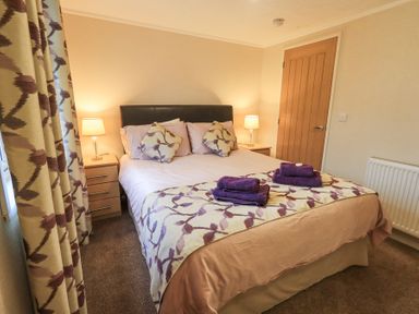 A bedroom with a double bed two bedside tables with lamps folded towels on the bed and a wooden door at Horseshoe Lodge Wansfell 5 Limefitt Park near Windermere