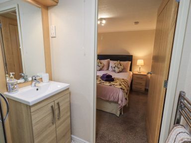 A bathroom sink with mirror and toiletries next to a bedroom with bed and nightstand lamp at Horseshoe Lodge Wansfell 5 Limefitt Park near Windermere