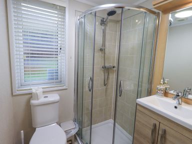 A bathroom with a toilet, a corner shower enclosure, and a sink with a mirror at Horseshoe Lodge in Wansfell 5 Limefitt Park near Windermere