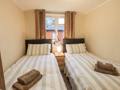 A bedroom with two single beds with striped bedding and brown towels on each bed at Horseshoe Lodge Wansfell 5 Limefitt Park near Windermere